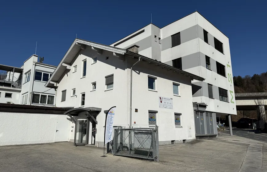 Auf dem Foto ist das weiße Gebäude zu sehen, in welchem der Brettspielverein Kufstein untergebracht ist. Links des Gebäude steht eine Fahne, bei welcher sich die Eingangstüre befindet.